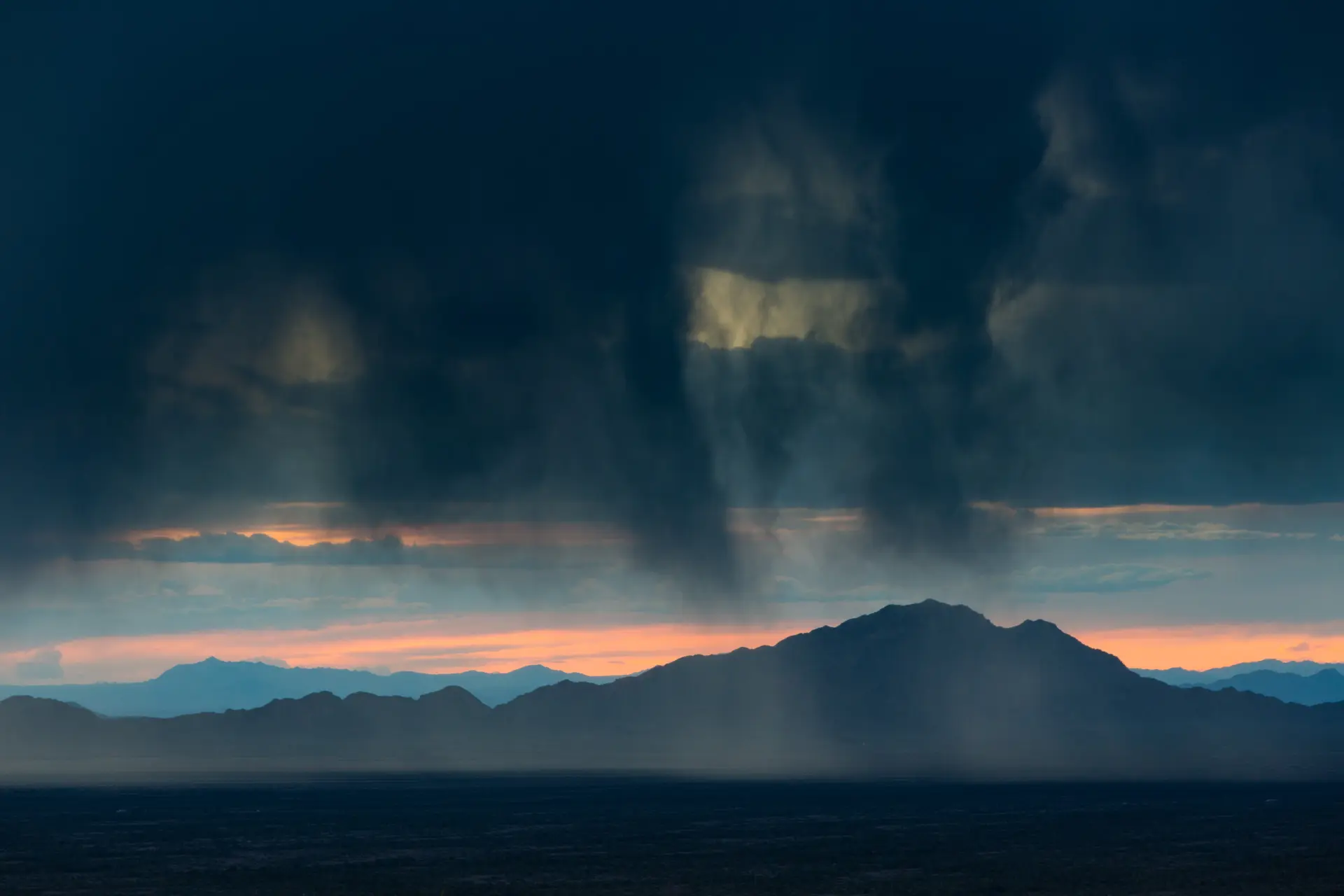Mountain Range in Silhouette against sunset with Rain Clouds in the Foreground